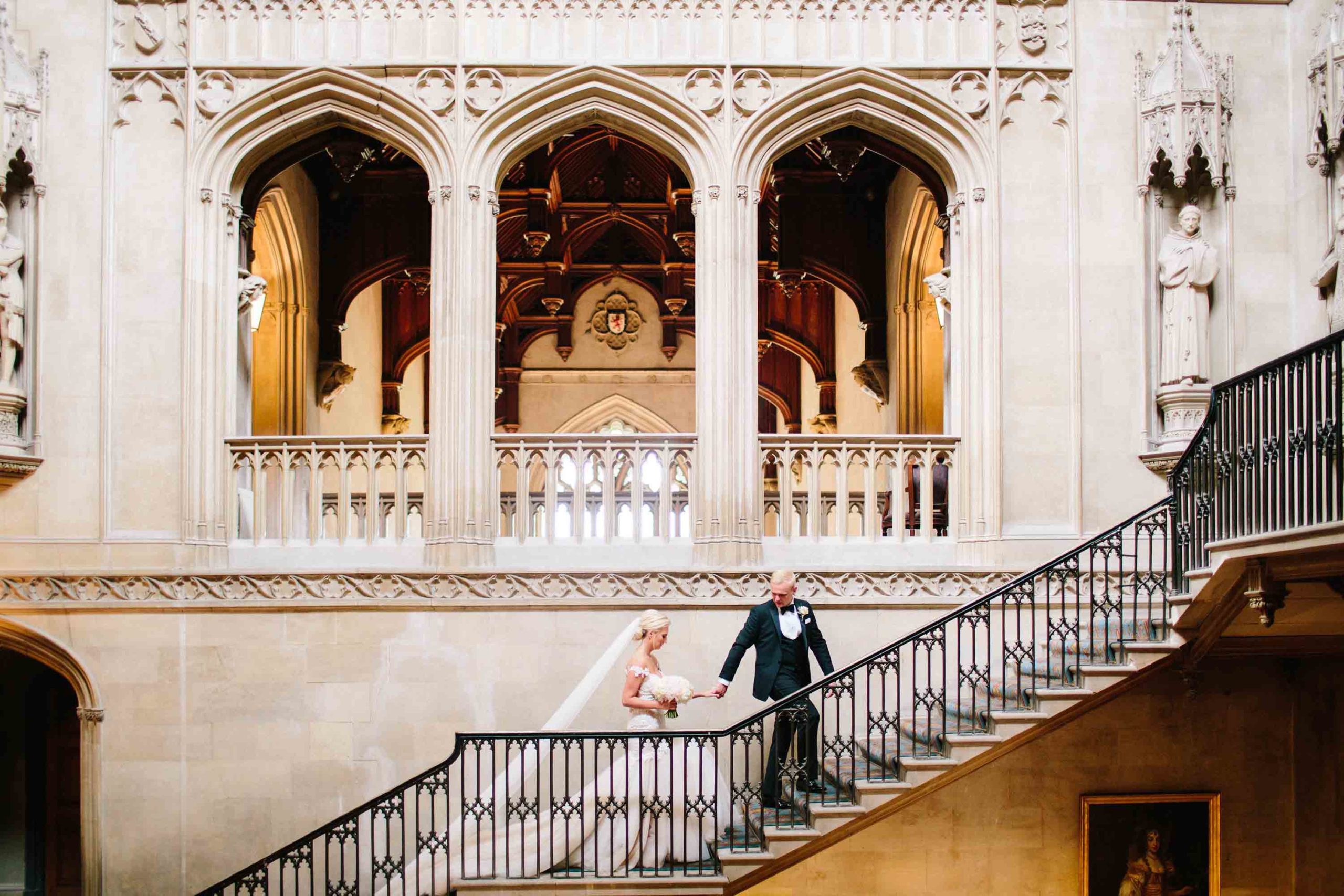 groom leading his bride up the main staircase at ashridge house after their wedding